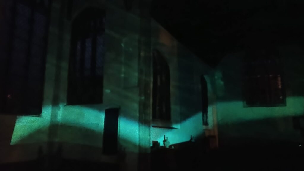 An image of the church interior in darkness, with a wave of blue/green light projected across the walls